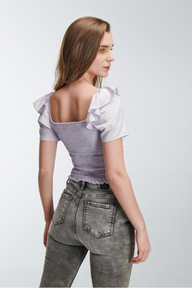 Blusa escotada y ajustada en tela fluida de color sólido, con hombros encauchados.
